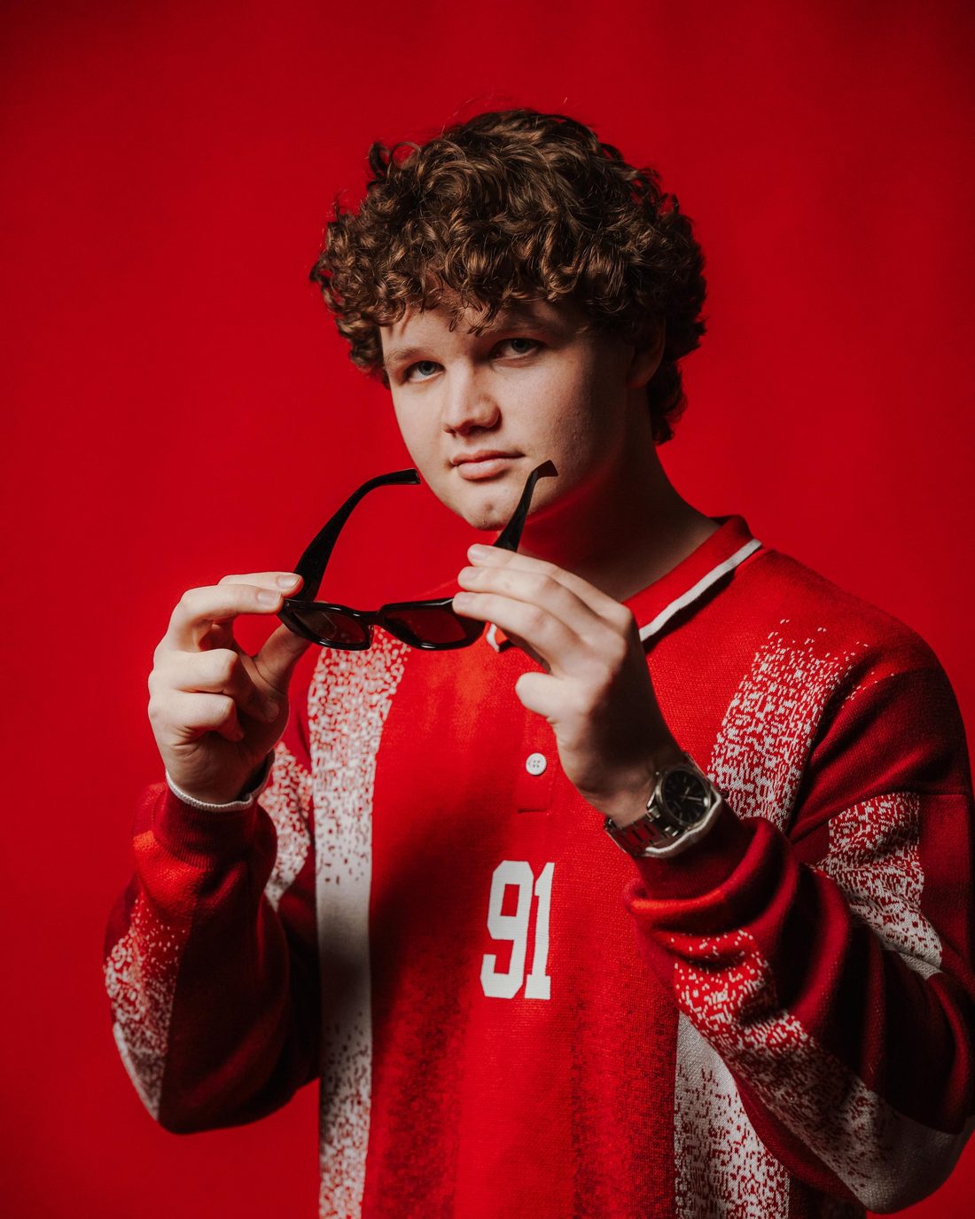 DENØO in a red 91 jersey, holding sunglasses